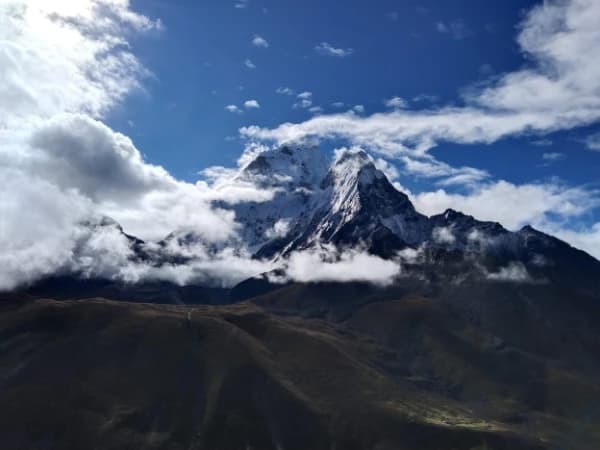 Tall rocky mountain with white snow patches and moving clouds across the summit.